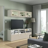 Soggiorno moderno con mobile tv bianco BESTÅ, divano grigio, tavolo in vetro, tende alte e design elegante.