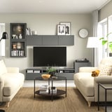 Soggiorno moderno con mobile tv BESTÅ grigio, divani bianchi con cuscini gialli, tavolino in vetro e lampada da terra nera.