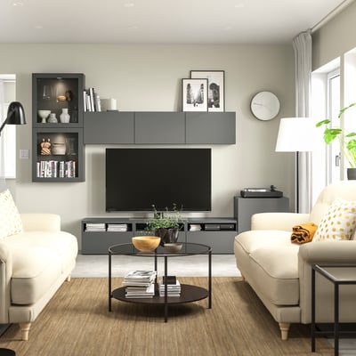 Soggiorno moderno con mobile tv BESTÅ grigio, divani bianchi, tavolino in vetro e oggetti decorativi.
