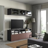 Soggiorno moderno con mobile tv BESTÅ nero, mensole e ante in vetro. TV a schermo piatto, oggetti decorativi e soluzioni di archiviazione.