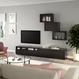 Soggiorno moderno con mobile tv BESTÅ, tv a schermo piatto, pensili, tavolino in vetro, divano beige, sedia, pianta e arte.