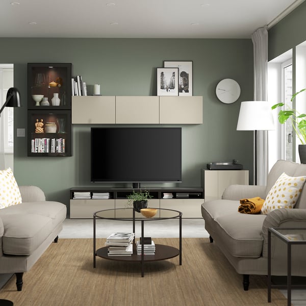 Soggiorno moderno con mobile tv BESTÅ, colori neutri, pareti verdi, pavimento in legno, due divani con cuscini a pois, un tavolo rotondo e una lampada alta.