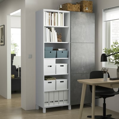 Mobile contenitore BESTÅ bianco per l'home office con ripiani misti aperti/chiusi, scrivania e sedia vicine. Camera luminosa con pavimento in legno.