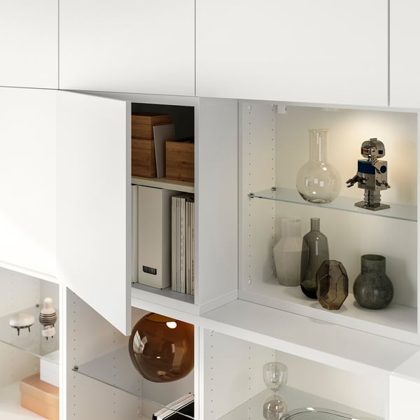 Scaffale moderno bianco con ante in vetro, raffigurante vari oggetti decorativi e libri, con ripiani regolabili.