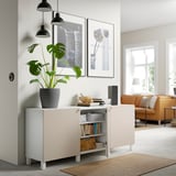 Soggiorno moderno con credenza BESTÅ, che espone libri, una pianta e opere d'arte incorniciate. Le cerniere soft-close sono evidenti sulle ante aperte dell'armadio.