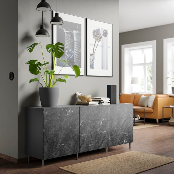 Soggiorno moderno con credenza BESTÅ in marmo grigio, con pianta alta, quadri incorniciati e divano arancione.