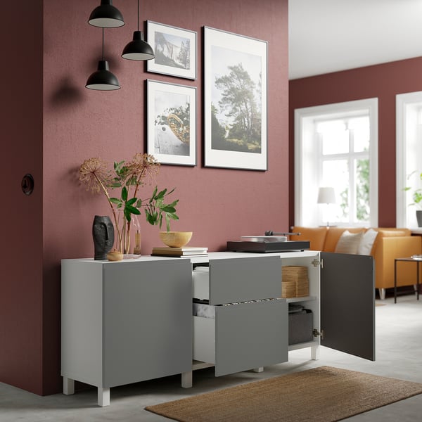 Soggiorno moderno con credenza BESTÅ grigia, decorato con vasi, fiori e foto incorniciate. Divano arancione nelle vicinanze.