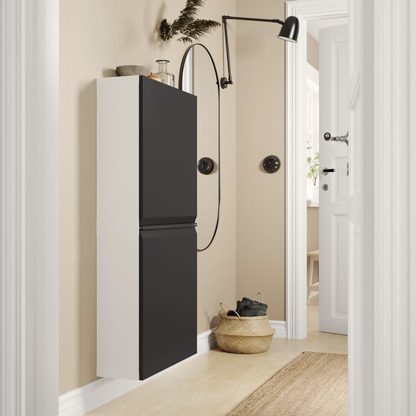 Moderno armadio in bianco e nero con maniglie eleganti, lampada a led integrata e cestino intrecciato sottostante, appoggiato a una parete di colore chiaro.