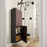 Camera moderna con mobile BESTÅ verde scuro a parete, porta a giorno che rivela libri e lampada da parete nera.