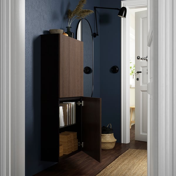 Armadietto con libri, cestini, lampada, vaso. Parete blu, porta luminosa.