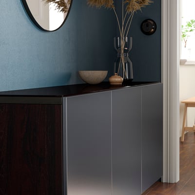 Piano di lavoro in vetro scuro sull'unità BESTÅ in una stanza moderna, che riflette la luce con oggetti decorativi.