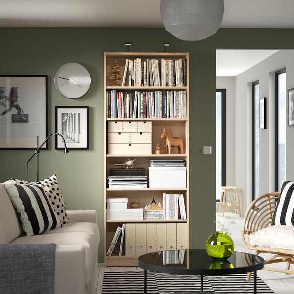 Elegante soggiorno con libreria BILLY tra divano bianco e sedia in legno, che contiene libri e decorazioni.