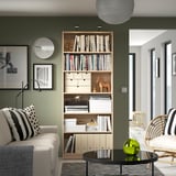 Elegante soggiorno con libreria BILLY tra divano bianco e sedia in legno, che contiene libri e decorazioni.
