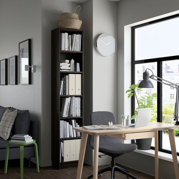 Home office moderno: libreria BILLY alta con libri, sedia grigia, piccolo sgabello verde, comodo divano, scrivania con laptop, grande finestra.