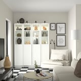 Soggiorno bianco moderno con librerie BILLY, tappeto a scacchi, tavolo beige, divano e lampada color crema.