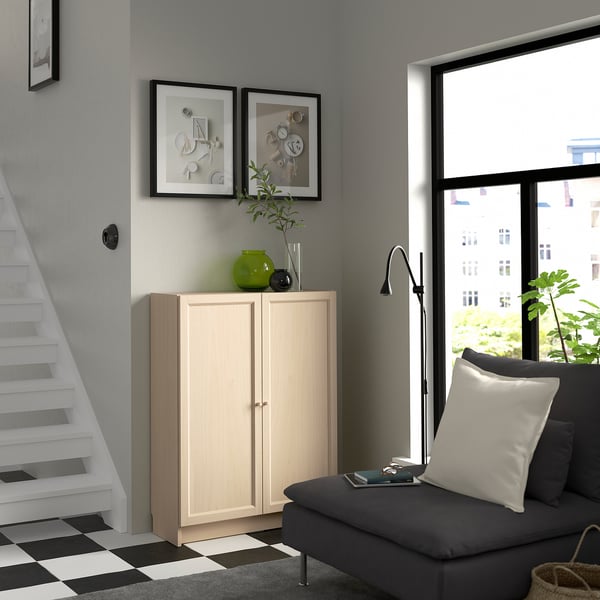 Libreria BILLY in legno tra scale e finestra, decorata con vasi e opere d'arte. Divano grigio con cuscino bianco nelle vicinanze.