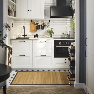 Cucina moderna con armadi bianchi, elettrodomestici neri e tappeto BLANGSLEV sotto il lavello.