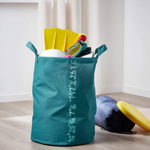 Borsa portaoggetti verde acqua con coordinate oceaniche, che tiene i giocattoli sportivi sul pavimento in legno chiaro.