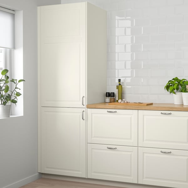 Cucina moderna con armadi BODBYN alti e bianco sporco. Due piante in vaso e bottiglie sul bancone. Pannelli lisci e smussati.