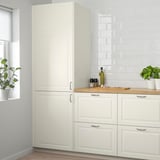 Cucina moderna con armadi BODBYN alti e bianco sporco. Due piante in vaso e bottiglie sul bancone. Pannelli lisci e smussati.