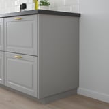Mobile da cucina grigio con maniglie dorate, due cassetti, piano di lavoro nero.