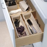 Il cassetto aperto mostra gli organizer BOLLÖSUND con accessori per capelli e spazzole, che separano ordinatamente gli oggetti per un facile accesso.