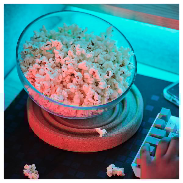 Una grande ciotola di popcorn si trova su un sottobicchiere intelligente, riducendo il rischio di fuoriuscite. Una mano tiene accanto un giocattolo in stile lego.