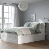 Letto BRIMNES bianco con contenitore in camera accogliente. Ampi cassetti, testiera alta, tende morbide ed elegante lampada.