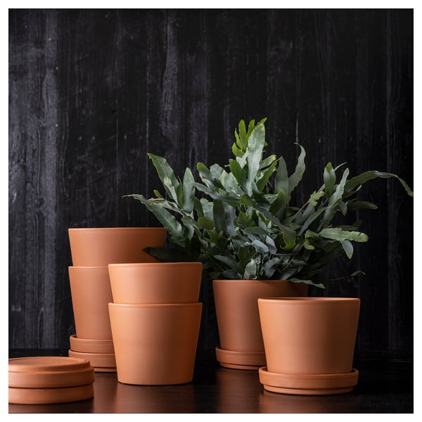 Vasi per piante BRUNBÄR in terracotta mostrati impilati in varie dimensioni su uno sfondo di legno scuro.