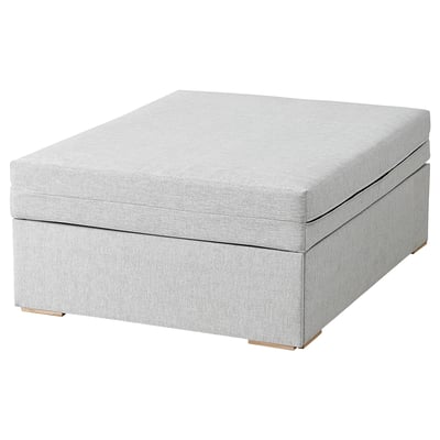 Un pouf in tessuto grigio chiaro che si trasforma in un letto. Ha un design moderno con linee pulite e gambe in legno.