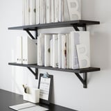 Mensole nere a muro con libri e oggetti decorativi. Include un blocco appunti con matite.