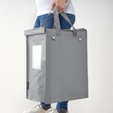 Persona che tiene la borsa DIMPA grigia per maniglie. La borsa è dotata di tasca trasparente per l'etichettatura, adatta per la raccolta differenziata.