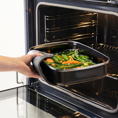 Una mano che tiene una teglia con le verdure, mettendola in un forno.