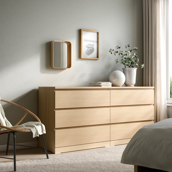 Camera da letto minimalista con mobili in rovere: specchio, comò, vaso, sedia, finestra.