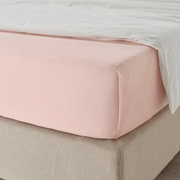 Un letto ben fatto con un lenzuolo rosa chiaro, leggermente stropicciato, su un materasso beige. Il lenzuolo è liscio e sembra essere di cotone.