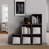 Scaffale modulare marrone scuro con contenitori in tessuto e libri, decorato con decorazioni, contro una parete grigia con un quadro incorniciato.