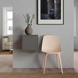 Camera minimalista con sedia in legno chiaro, pianta, tavolino grigio e opere d'arte incorniciate.
