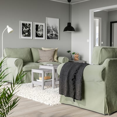 Accogliente soggiorno con divani EKTORP verde chiaro, opere d'arte in bianco e nero e una lampada a sospensione nera, che creano uno spazio moderno ma invitante.