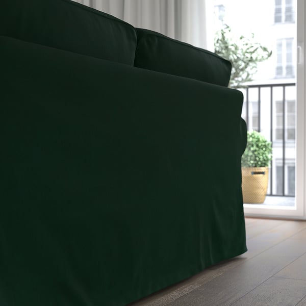 Divano EKTORP verde scuro vicino alla finestra, con piante rigogliose all'esterno.