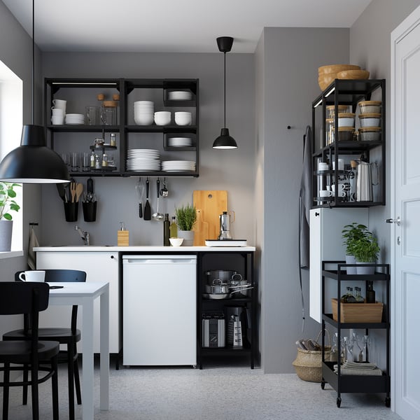 Piccola cucina moderna con armadi bianchi, sedie nere e scaffali che espongono piatti e oggetti da cucina.