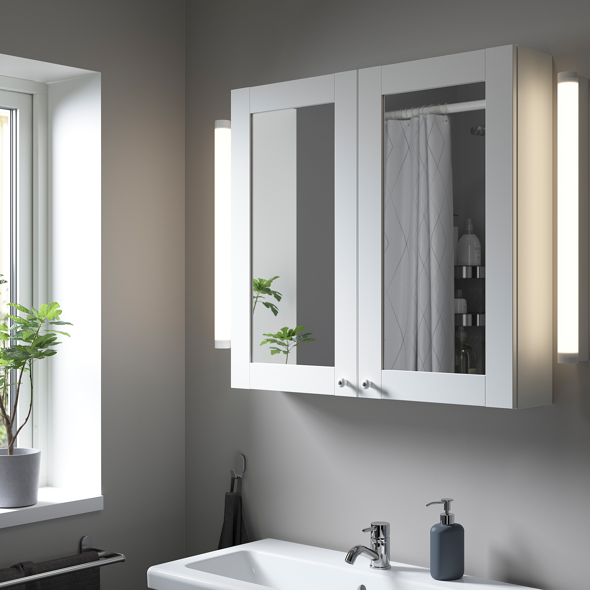 Bagno moderno con pensile bianco ENHET. Le grandi ante a specchio valorizzano lo spazio; case articoli da toeletta. Parete grigia e lavandino sottostante.