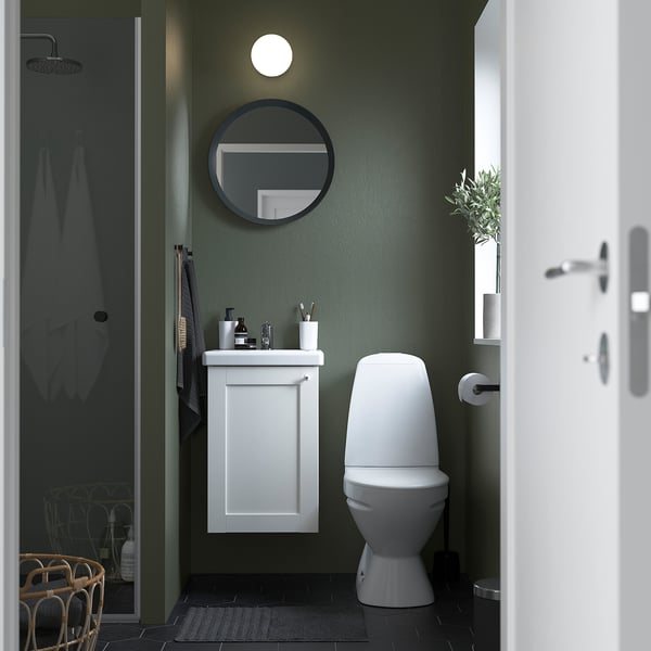Un bagno compatto con mobile ENHET, lavabo, specchio rotondo, WC e porta doccia in vetro.