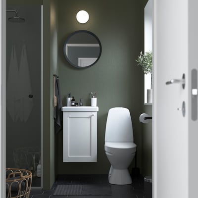 Un bagno compatto con mobile ENHET, lavabo, specchio rotondo, WC e porta doccia in vetro.