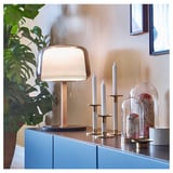 Elegante lampada moderna, colore oro, vetro e ottone. Su armadio blu, piante e decorazioni nelle vicinanze.