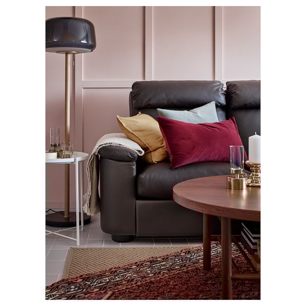 Soggiorno moderno con divano in pelle grigio scuro, cuscini colorati, tavolino in legno ed elegante lampada da terra.