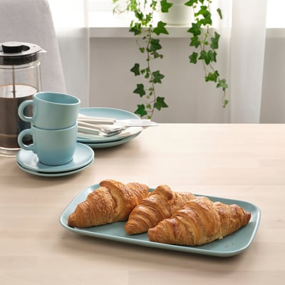Set da tavola in legno chiaro con piatti, tazze e posate FÄRGKLAR azzurri; Pasticcini francesi su un piatto, caffè in una caffettiera francese.