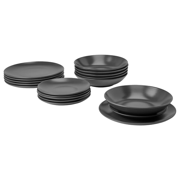 Un set di stoviglie FÄRGKLAR nere con piatti e ciotole, realizzate in gres con finitura opaca, disposte in modo ordinato.