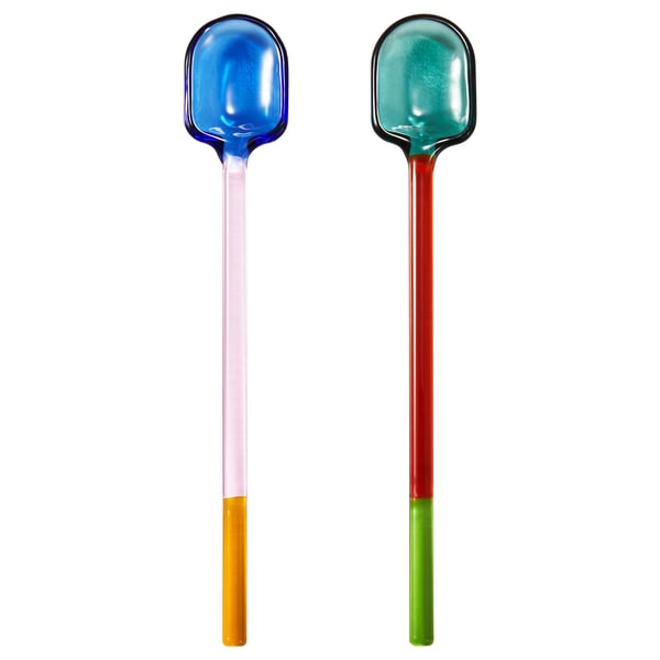 Due cucchiai di vetro multicolori con bordi arrotondati e diversi colori del manico, che apparecchiano una tavola giocosa.
