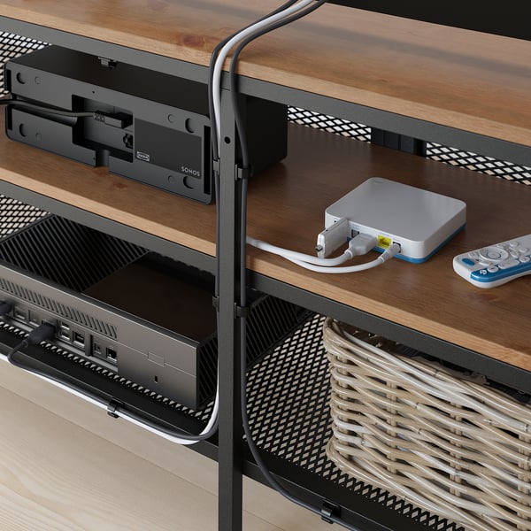 Porta tv in legno con ripiani in rete metallica, ospita una console di gioco e telecomandi. I piedini regolabili garantiscono stabilità.