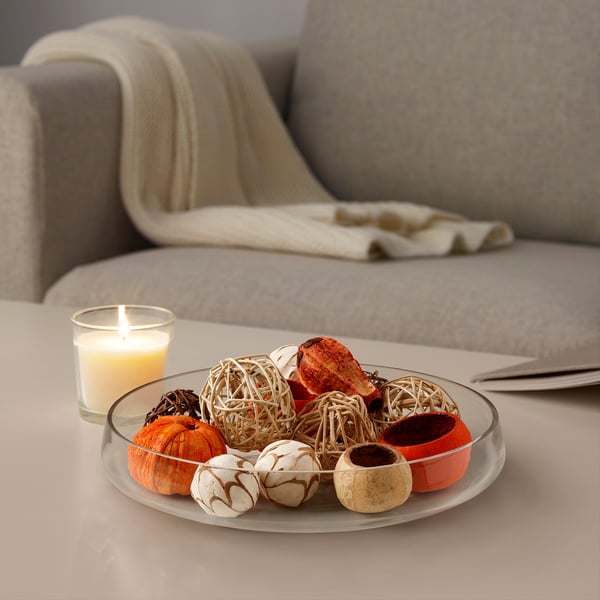 Soggiorno con candela accesa, decorazione autunnale in ciotola di vetro sul tavolo prima del divano grigio con coperta.